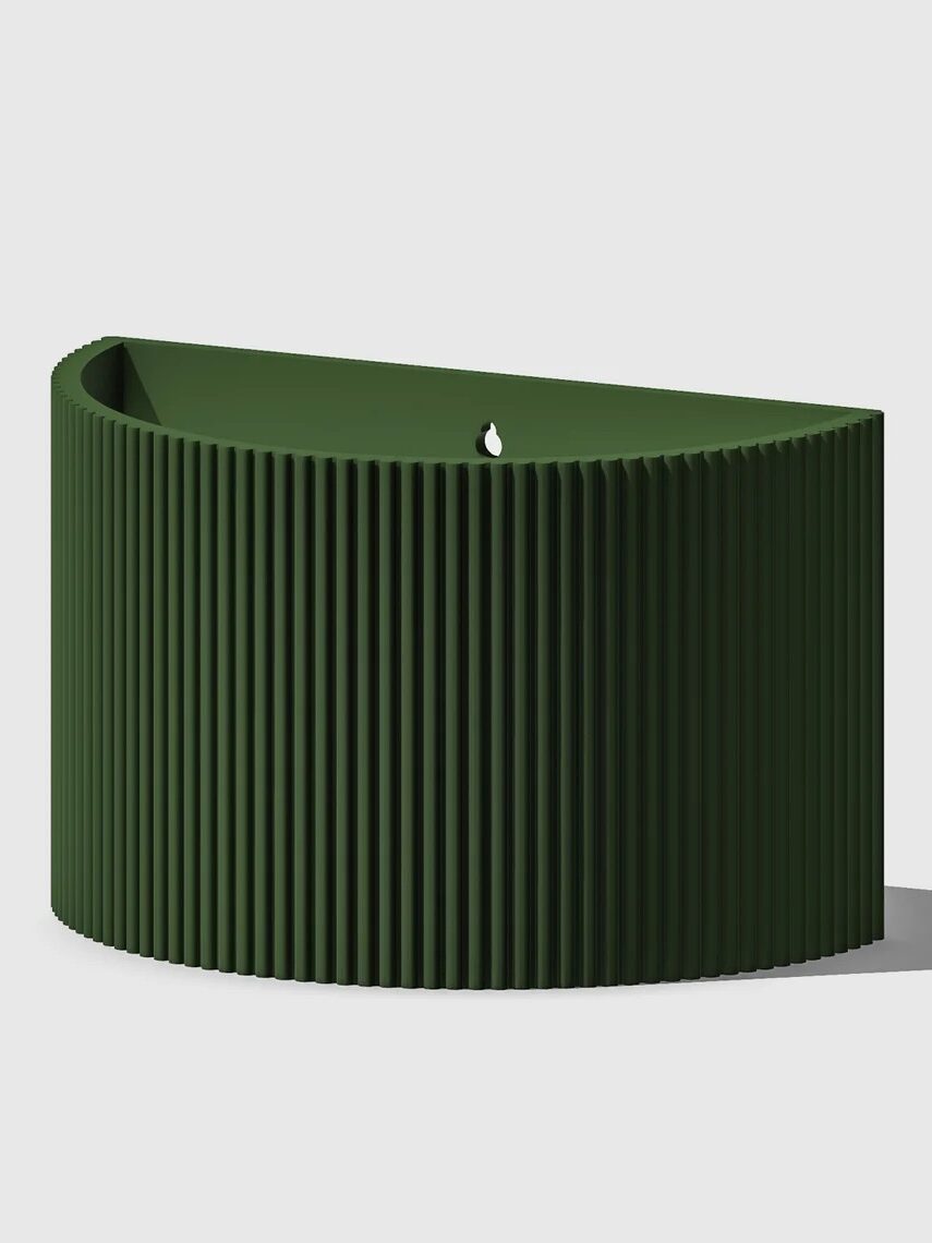 A green, semi-circular, ribbed planter with a drainage hole, casting a shadow on a light background.