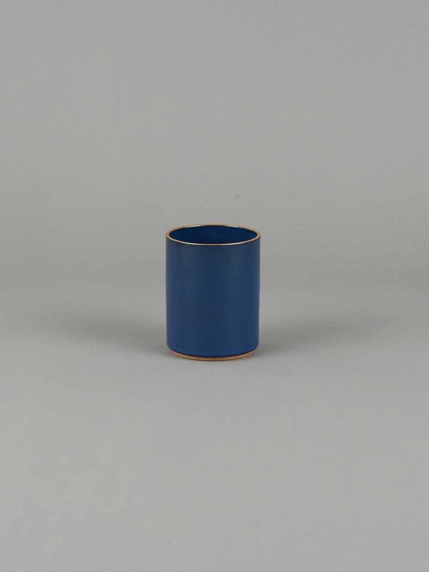 A small, cylindrical blue ceramic cup with a smooth surface, placed on a plain gray background.