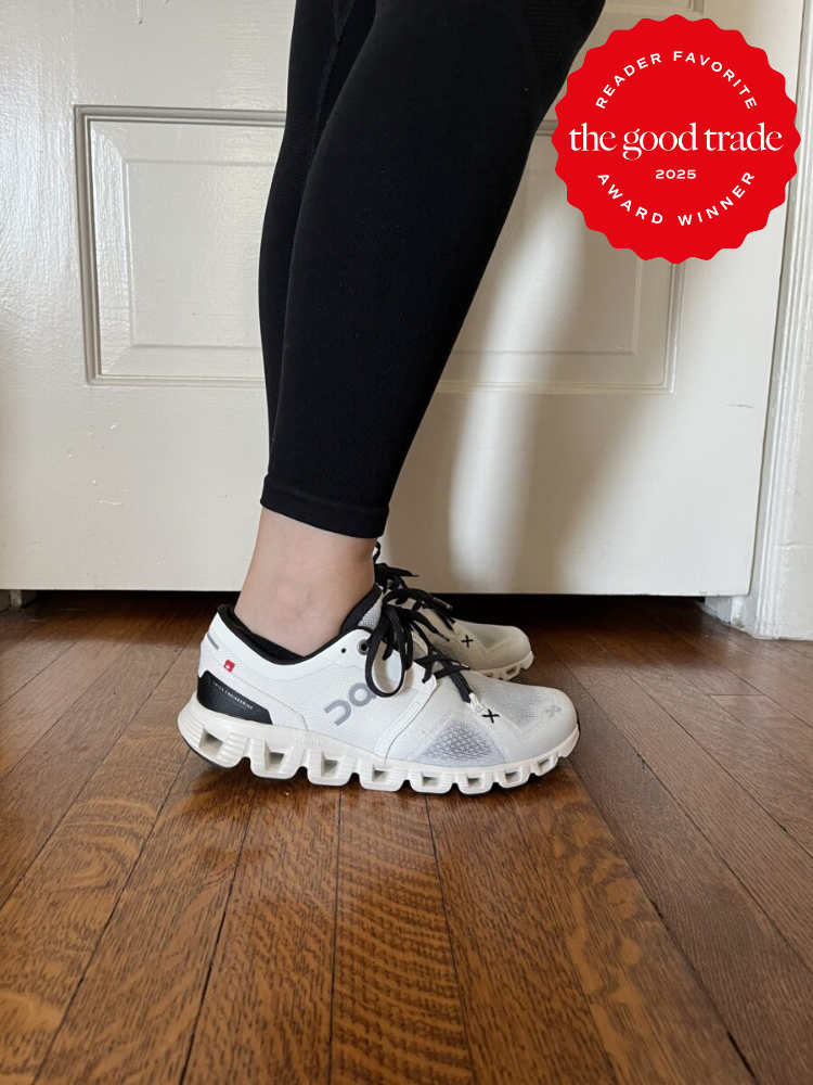Person wearing black leggings and white sneakers with black laces standing on wooden floor. A red badge on the image reads "Reader Favorite, the good trade, Award Winner, 2025.