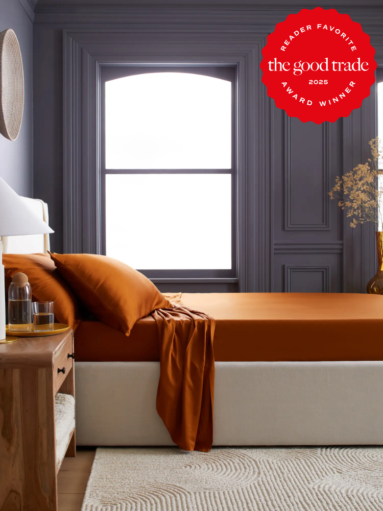 A bedroom with a bed featuring brown sheets and a wooden side table. A window with centered arch is in the background. A red award badge is in the top right corner.