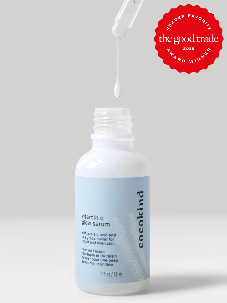 A pipette drips a white liquid into an open bottle labeled "cocokind vitamin c glow serum." A red award badge is in the top right corner.
