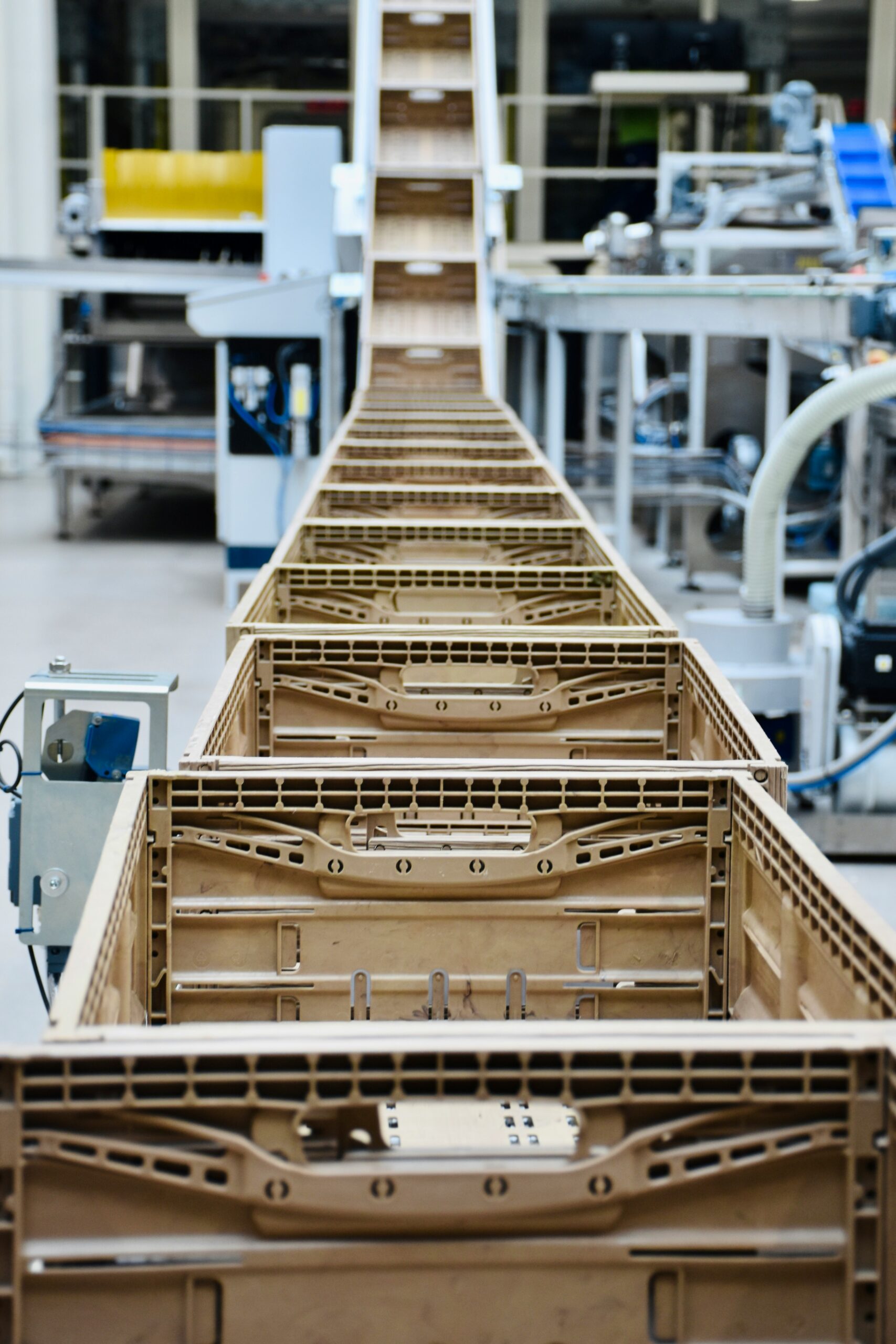 A long wooden frame structure in a factory setting, viewed from the end, with machinery and equipment in the background.