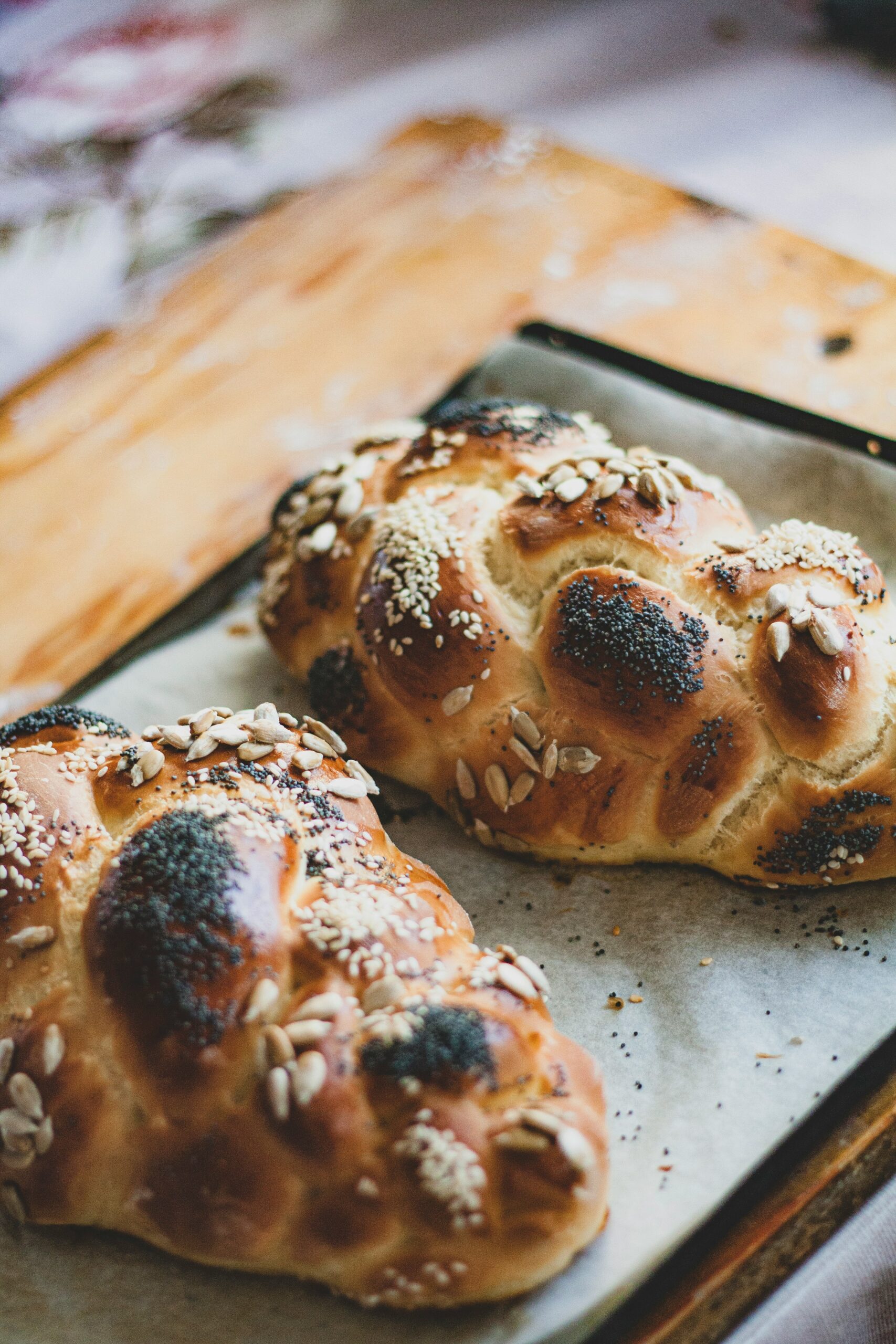 Two braided loaves of bread with sesame and poppy seeds, resting on a baking tray lined with parchment paper.