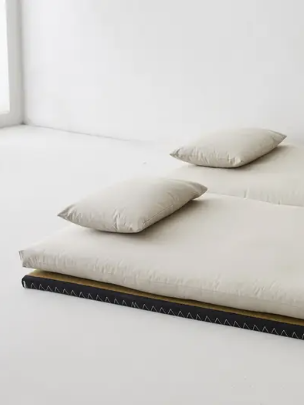 Two adjacent futons with white mattresses and pillows on a tatami mat in a minimalistic, bright room.