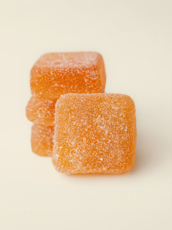 Stacked orange gummy squares coated with sugar on a light background.