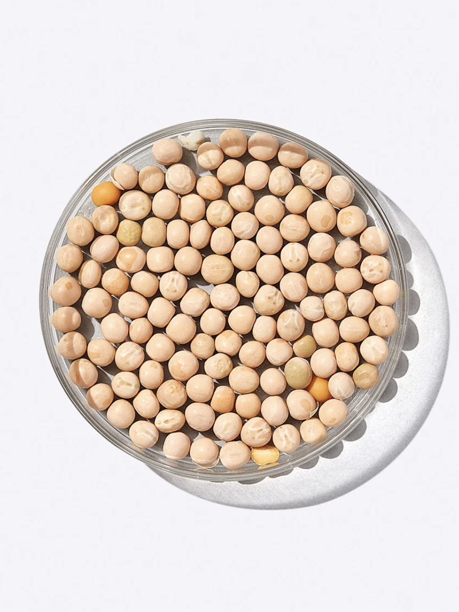 A clear glass bowl filled with round, beige chickpeas on a white background.