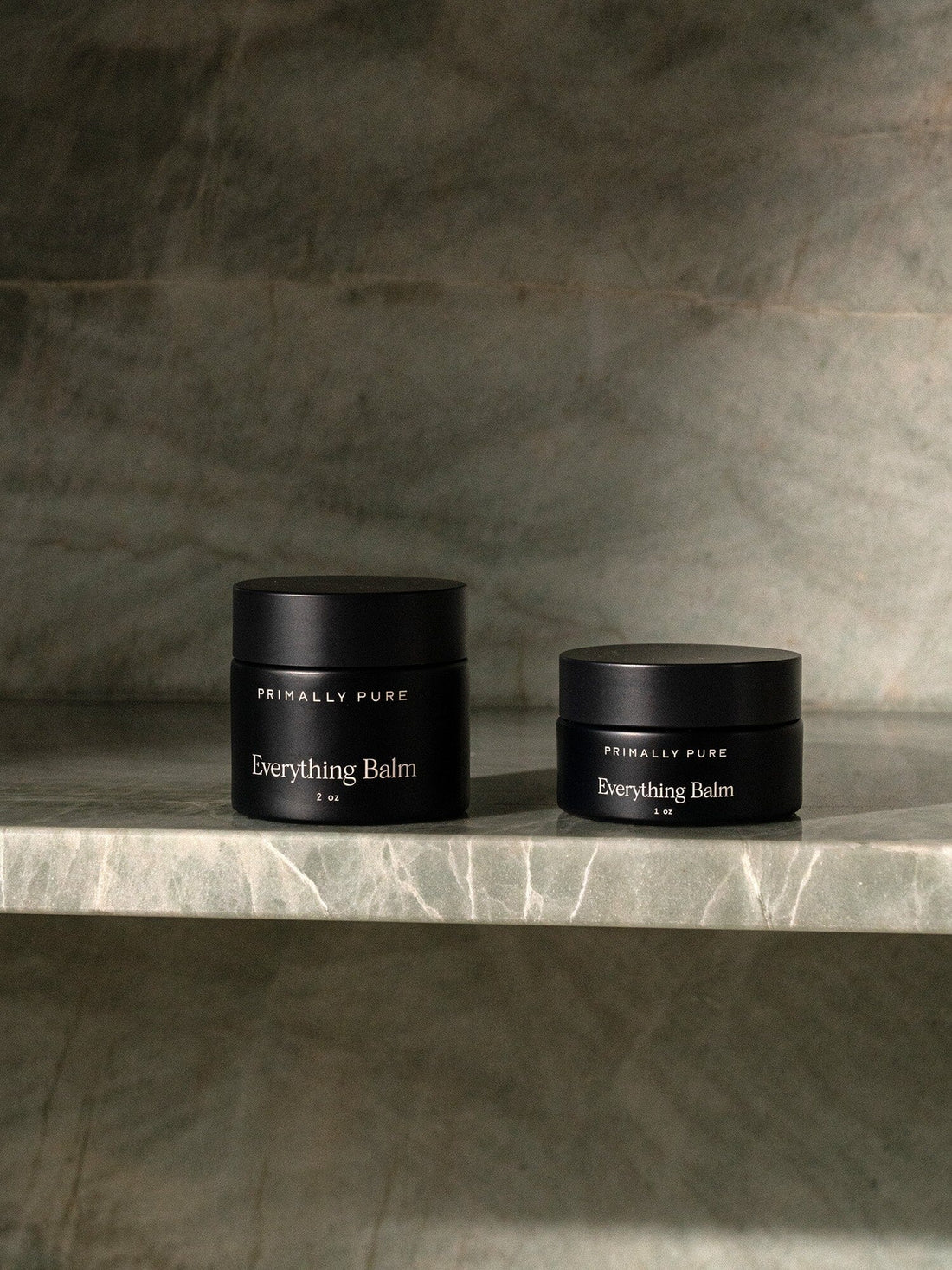 Two black jars of Primally Pure Everything Balm placed on a marble surface.