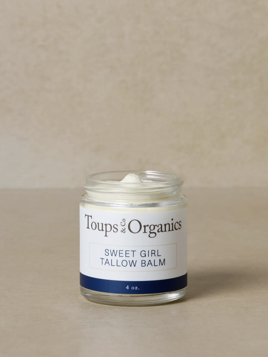 A jar of Toups and Co Organics Sweet Girl Tallow Balm with a white cream inside, placed on a neutral surface.