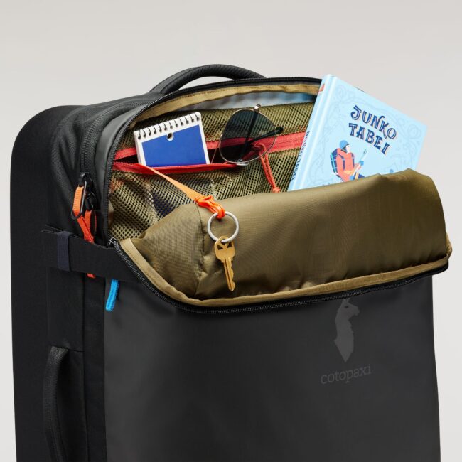 Open backpack with a book, sunglasses, notebook, and a key in the front pocket.