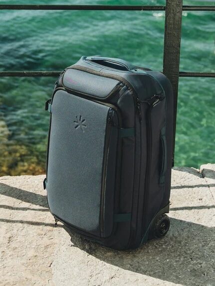 A black rolling suitcase stands on a concrete surface next to a railing, with clear green water in the background.