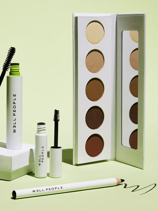 Cosmetics set including mascara, eyeliner, and an eyeshadow palette against a light green background.