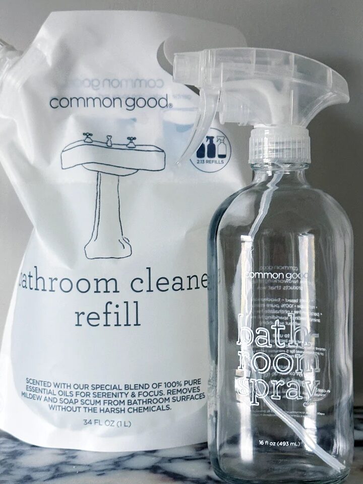 Bathroom cleaner products on a marble surface include a spray bottle labeled "bathroom spray" and a refill pouch labeled "bathroom cleaner refill.