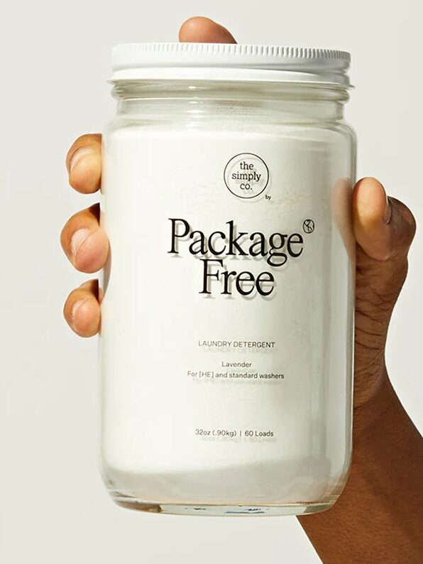 A hand holding a jar of Package Free laundry detergent against a light background. A green EWG Verified logo is visible in the top right corner.