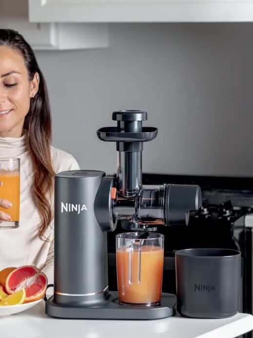 A person sits at a kitchen counter with a glass of orange juice beside a juicer machine. Sliced citrus fruits are on a plate. Text reads: "Real, fresh juices. Extract and enjoy pure fruit juice without the additives.