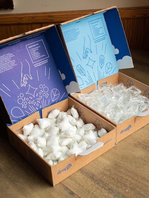 Three open boxes containing white and transparent pods. Packaging features blue designs with text and graphics. Boxes are placed on a wooden surface.