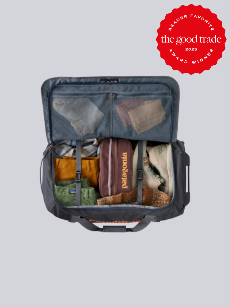 Open travel bag showing neatly packed clothing, shoes, and accessories. Red "The Good Trade 2025 Award Winner" badge at the top right corner.