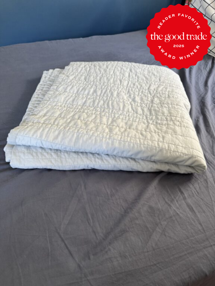 A folded, white quilt lies on a bed with gray sheets. A red badge in the top right corner reads "Reader Favorite, the good trade, Award Winner, 2025.