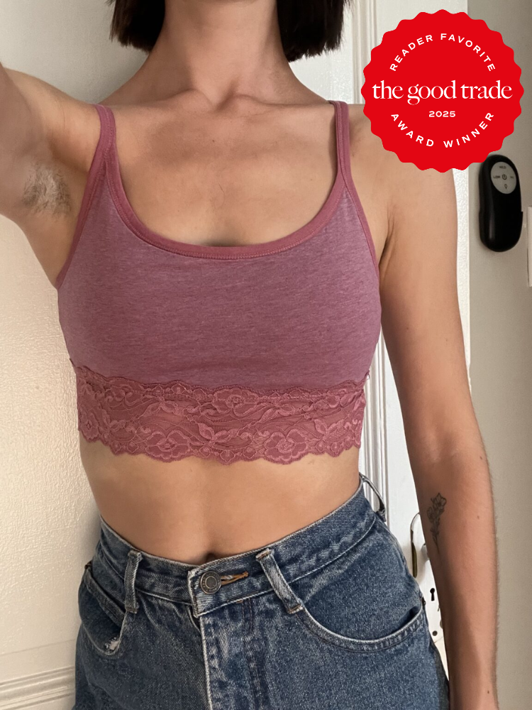 Person wearing a pink lace-trimmed tank top and blue jeans, standing indoors. There is a "Reader Favorite The Good Trade 2025 Award Winner" badge in the upper right corner.