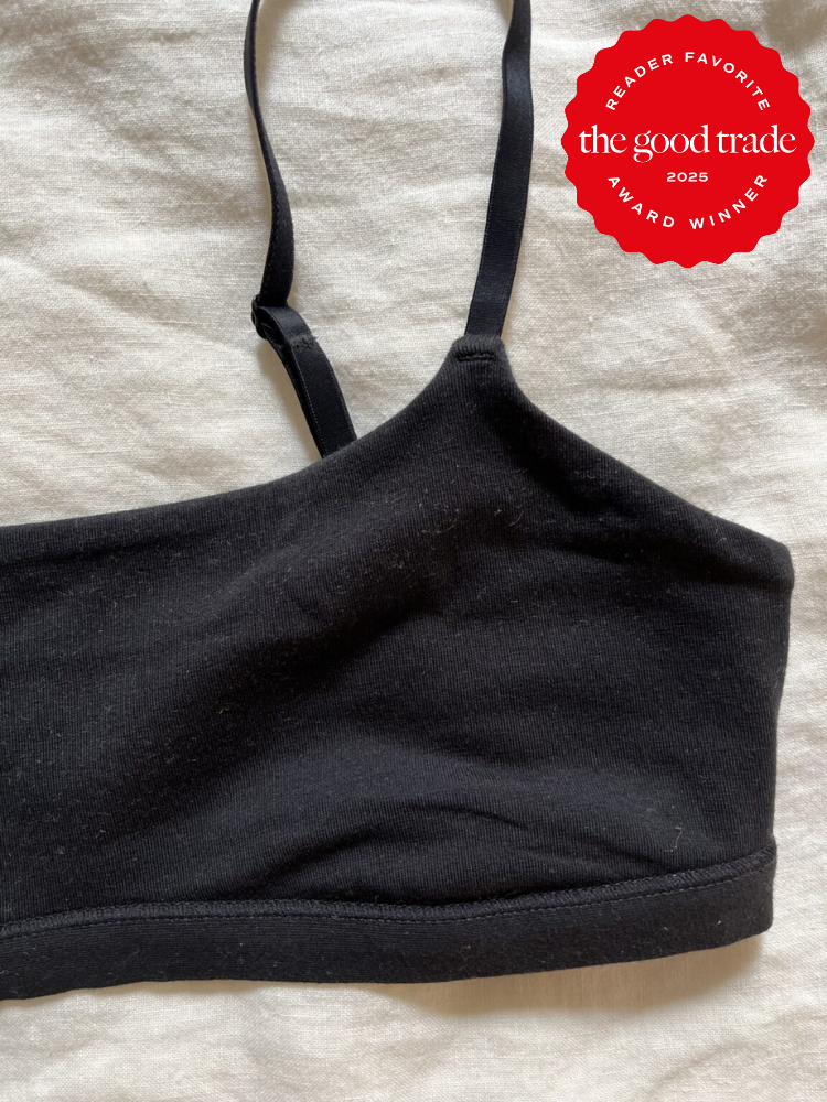 A black bralette with thin straps lays on a light fabric surface. A red badge in the corner reads "Reader Favorite The Good Trade Award Winner 2025.