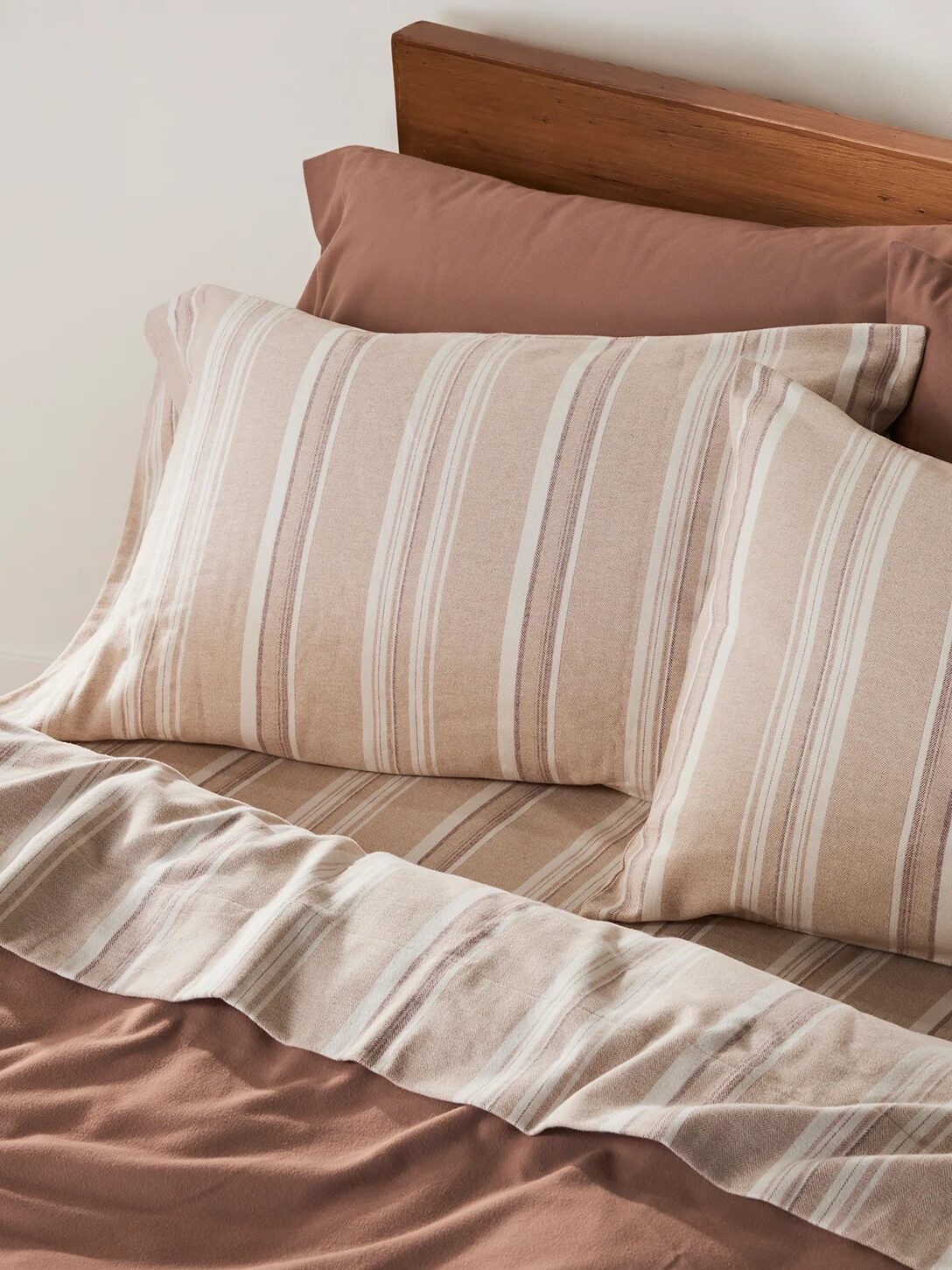 A neatly made bed with two striped pillows and matching striped sheets, set against a wooden headboard.