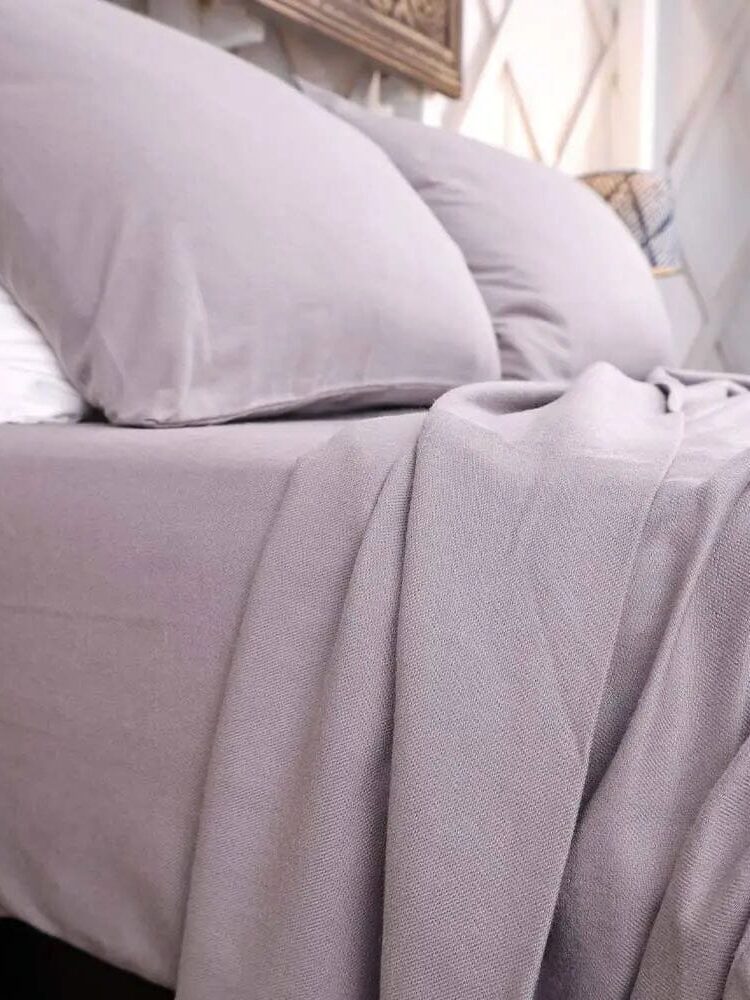Gray bed with neatly arranged pillows and a draped blanket in a bedroom setting.