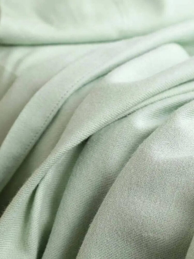 Close-up of soft, light green fabric with smooth folds and visible stitching details.