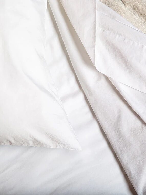 Close-up of neatly arranged bedding with a white pillow, white sheets, and a beige blanket in the corner.