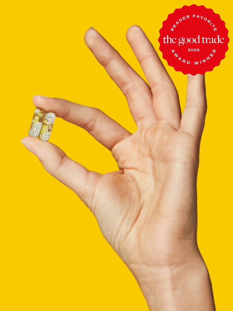A hand holds two clear capsules filled with small white granules against a yellow background. A red badge on the top right reads "The Good Trade 2025 Reader Favorite Award Winner".