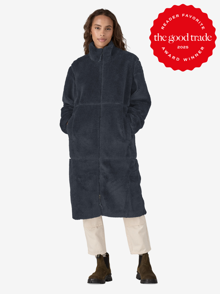 Person in a long, dark blue fuzzy coat with hands in pockets, light pants, and brown boots. A red "The Good Trade 2025 Reader Favorite Award Winner" badge is displayed.