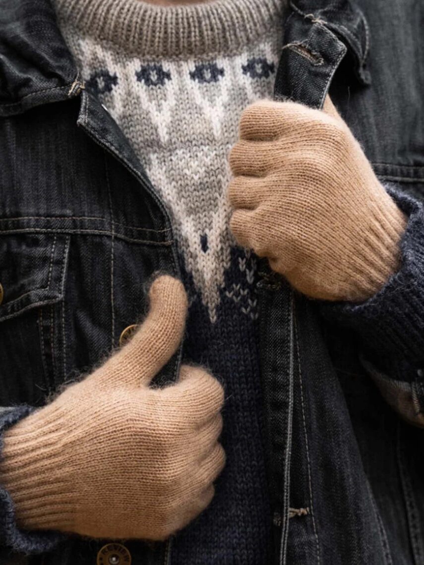 Person wearing a denim jacket and patterned sweater, adjusting the jacket with hands covered in beige knit gloves.