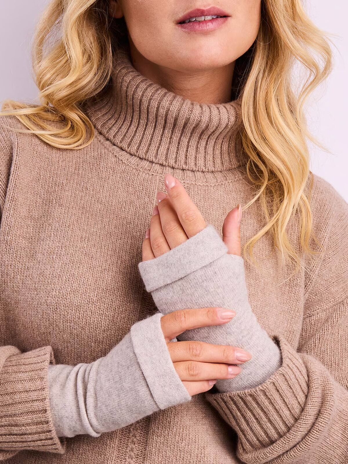 Person wearing a beige turtleneck sweater and gray fingerless gloves, with their hands clasped together.