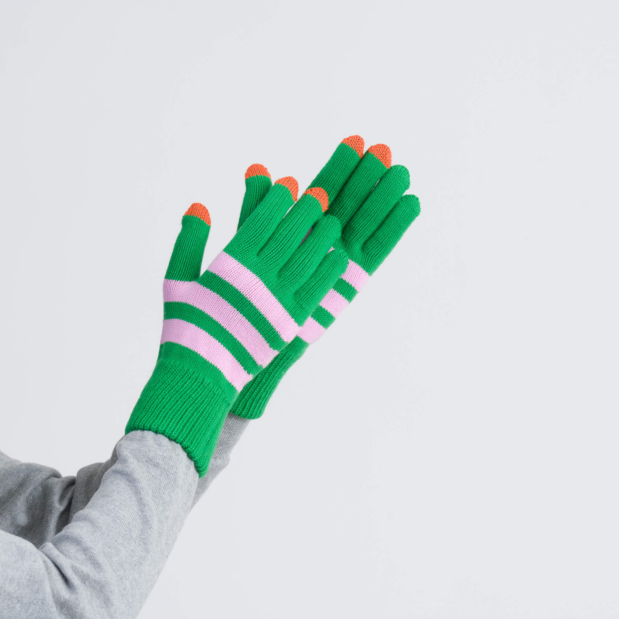 Hands wearing green gloves with pink and white stripes and orange fingertips against a plain background.