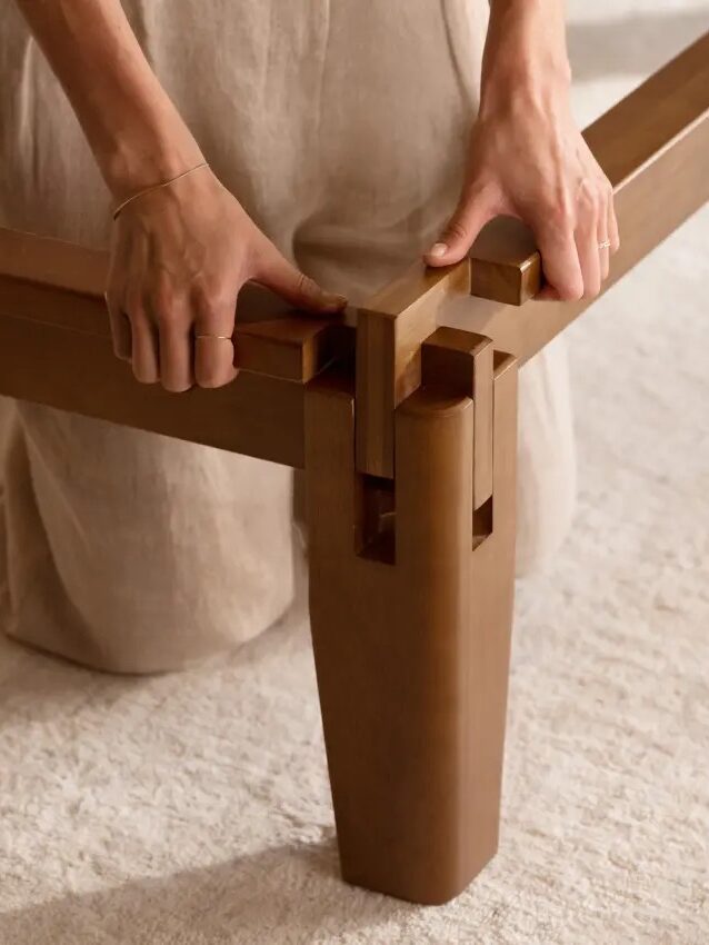 A person assembles a wooden frame by fitting a joint together on a carpeted floor.