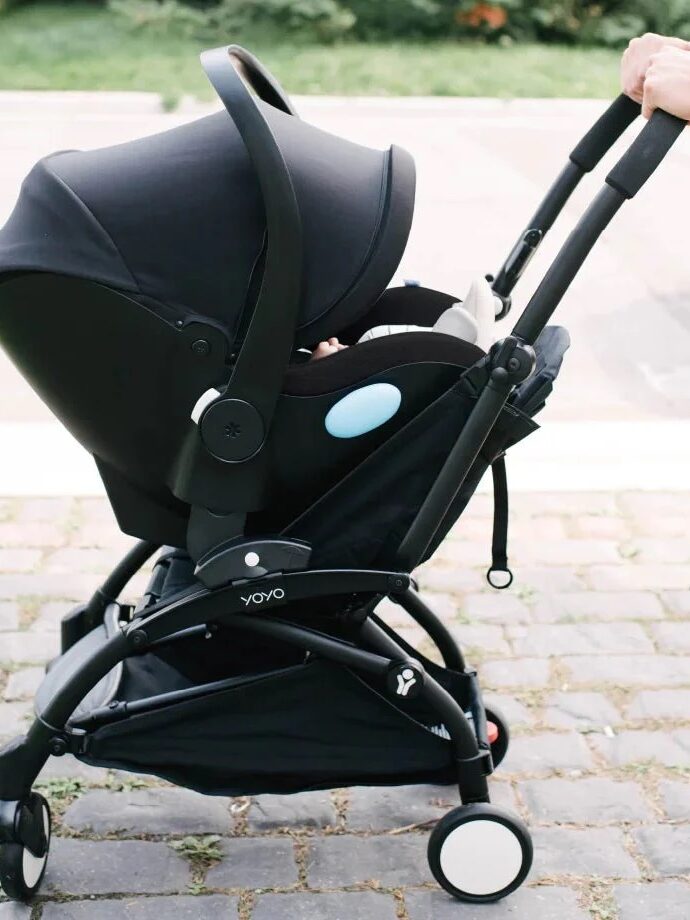 A person pushes a black baby stroller on a cobblestone path outdoors.