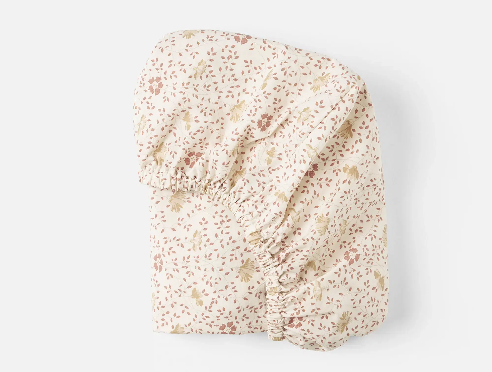 Beige fitted sheet with a small, scattered leaf and dot pattern in muted pink and green colors, folded on a white background.