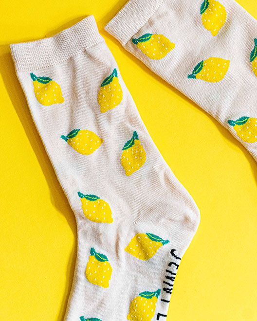 Organic socks featuring white fabric adorned with playful lemon patterns scattered on a vibrant yellow background.