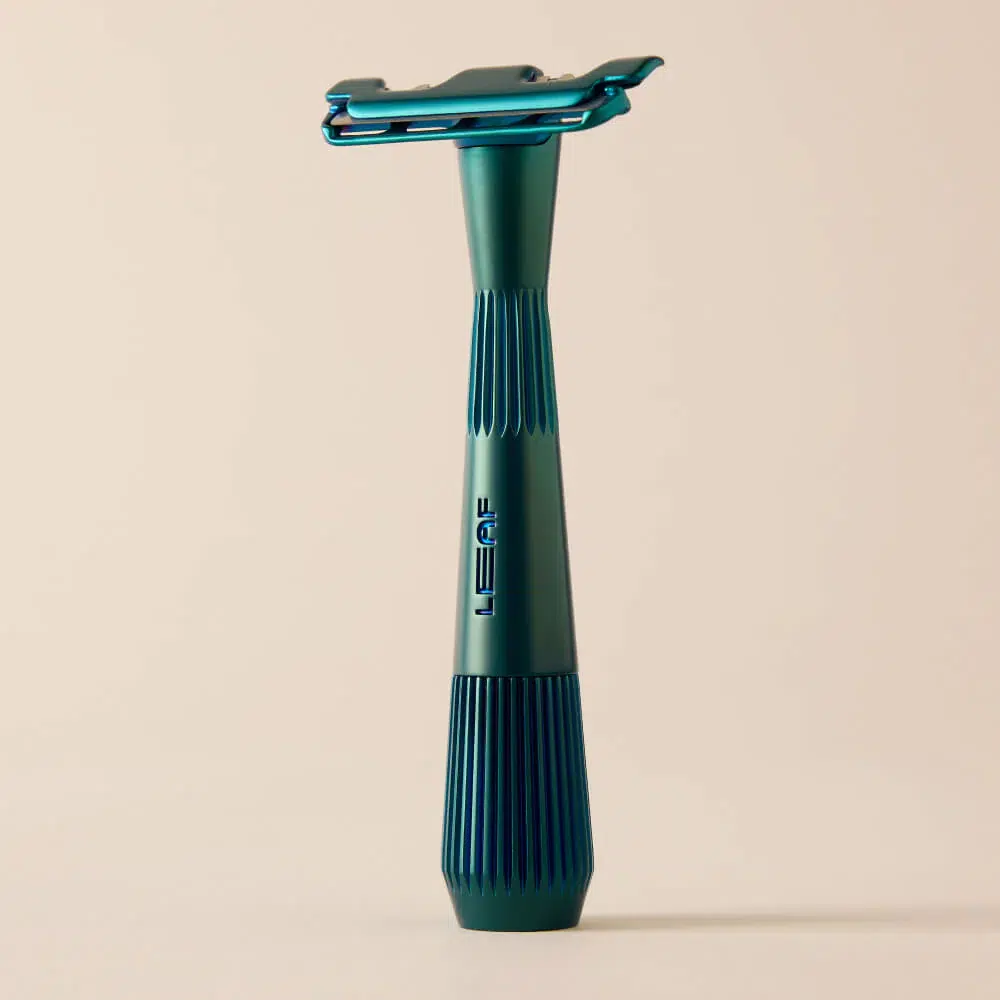 Teal-colored metal safety razor standing upright on a neutral background, featuring the brand name "Leaf" on its handle.