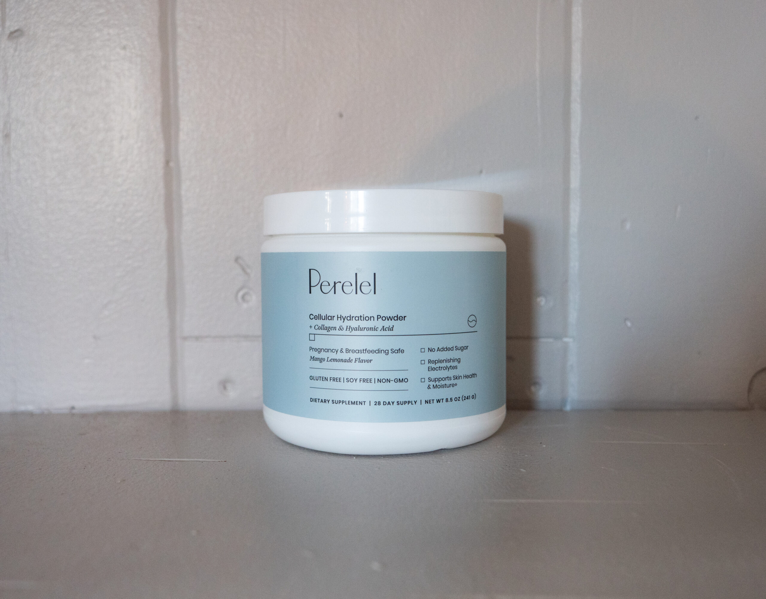 A white container of Perelel Cellular Hydration Powder on a gray surface, featuring collagen and hyaluronic acid. The label highlights benefits like skin elasticity and hydration.