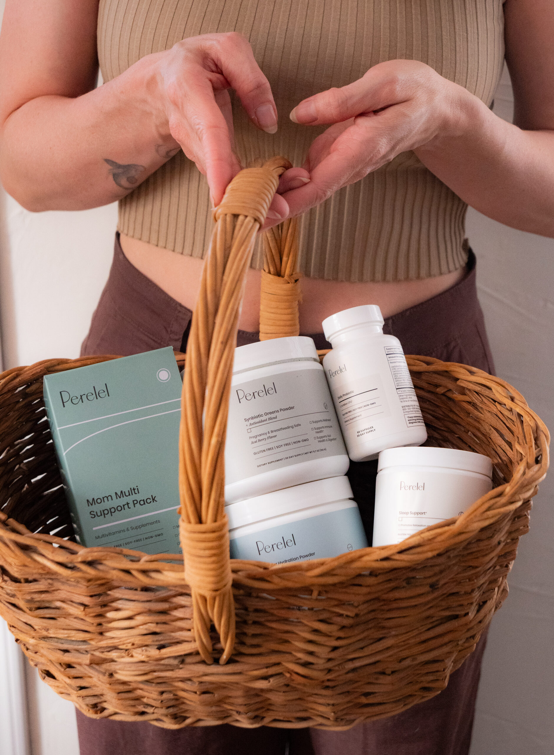Person holding a wicker basket containing several bottles and a box labeled "Mom Multi Support Pack" from Perelel.