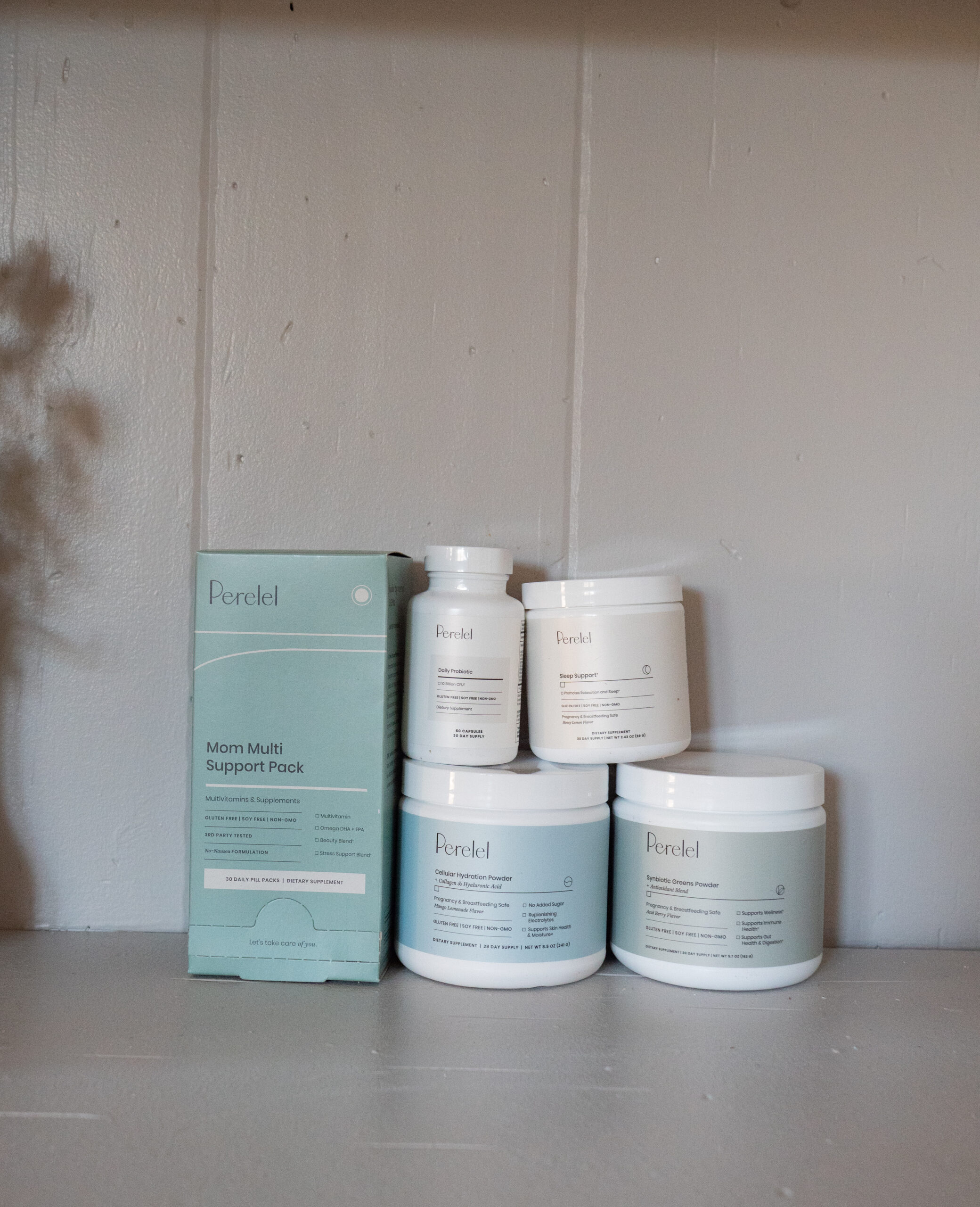 A set of Perel packaged wellness products, including a teal box labeled "Mom Multi Support Pack" and four containers, arranged on a neutral-colored shelf.