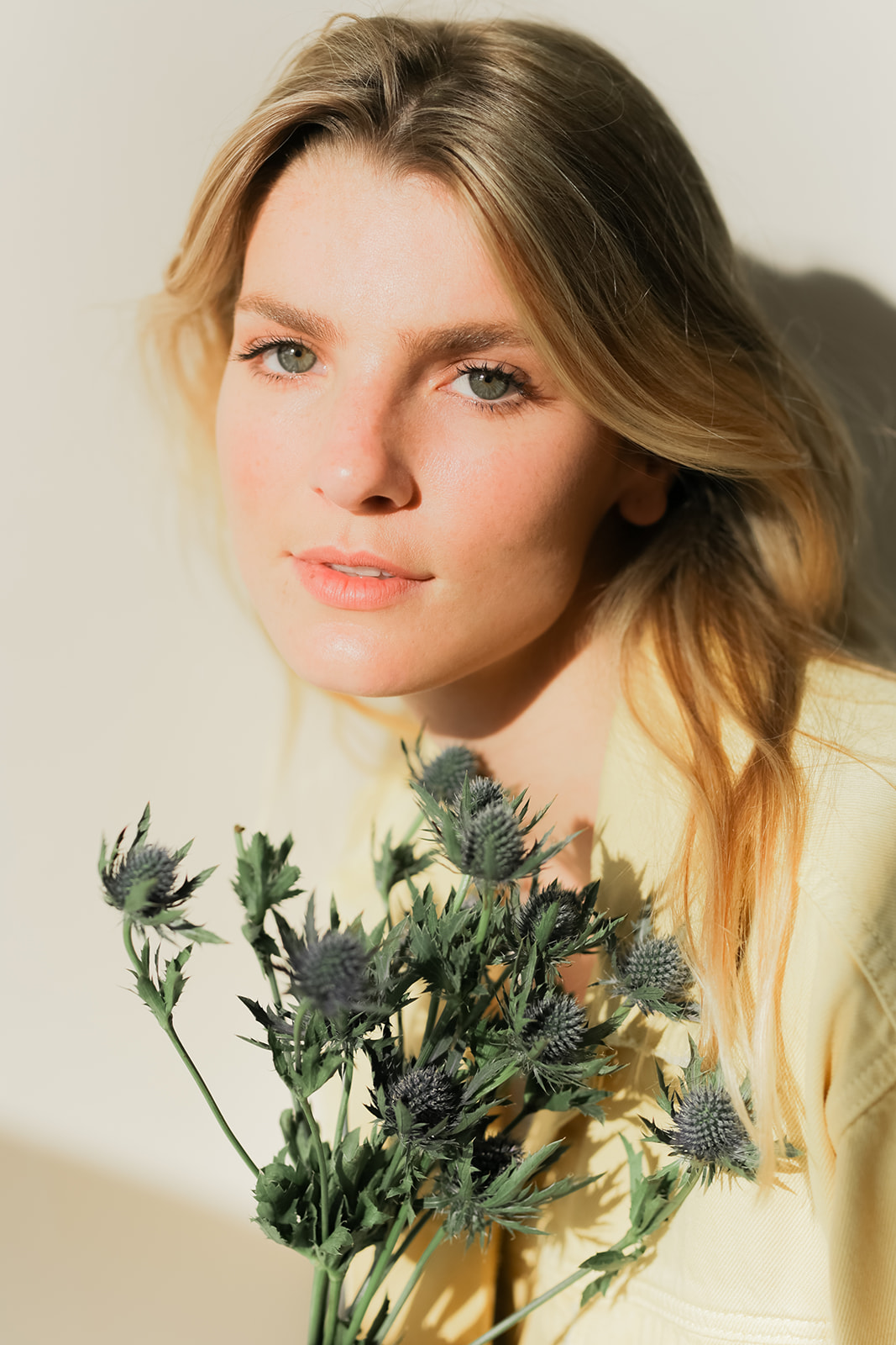 Person with long hair holding a bunch of thistle flowers, standing against a plain background.