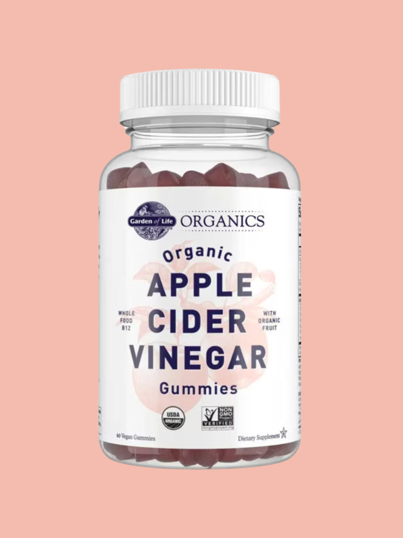 A bottle of Garden of Life brand organic apple cider vinegar gummies against a pink background.