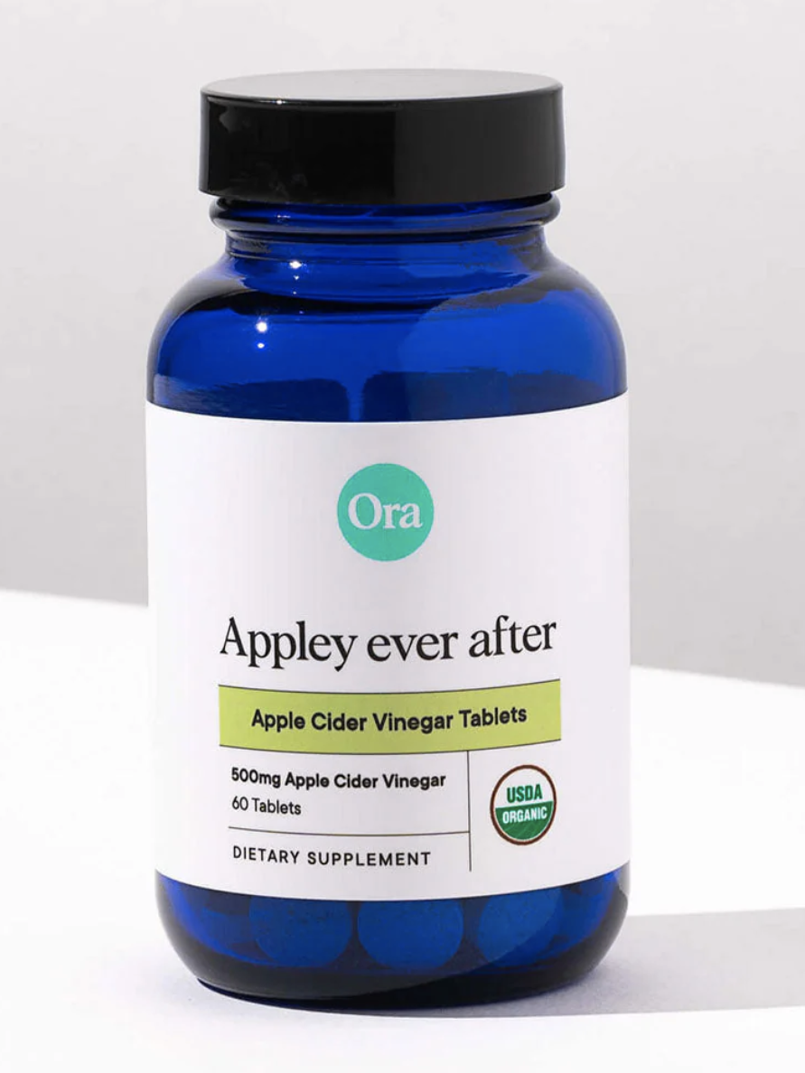 Blue bottle labeled "Ora Appley ever after," featuring apple cider vinegar tablets, 500mg, 60 tablets, USDA organic badge, on a light background.
