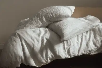 Two white quilted pillows rest on an unmade bed with a white blanket in natural light.