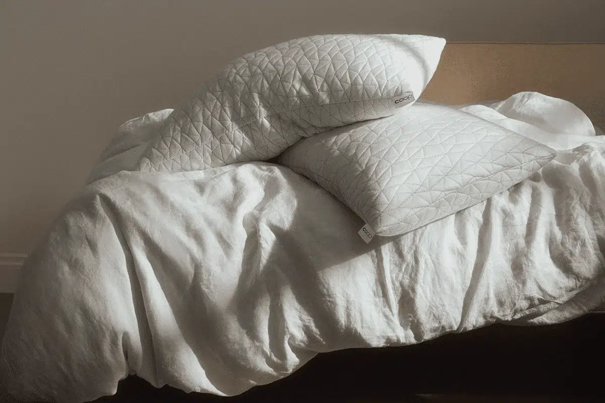 Two white quilted pillows rest on an unmade bed with a white blanket in natural light.