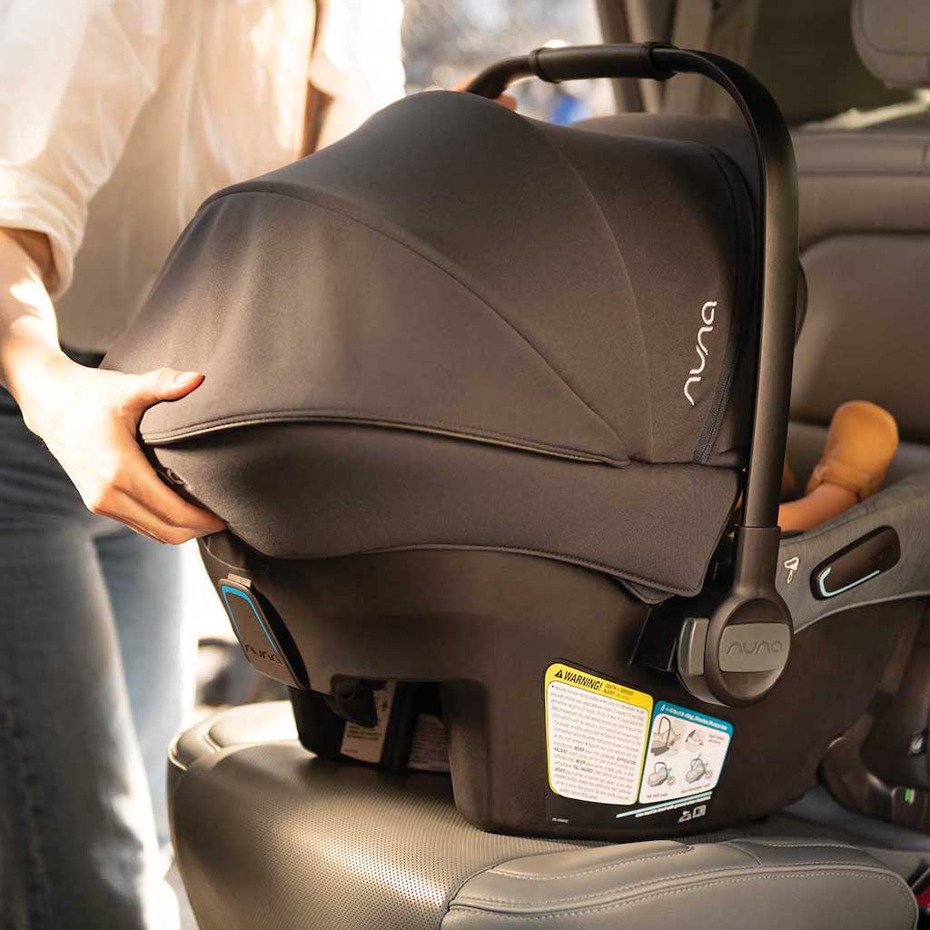 Person placing a black Nuna infant car seat with a canopy on a car seat, ensuring it is secure.