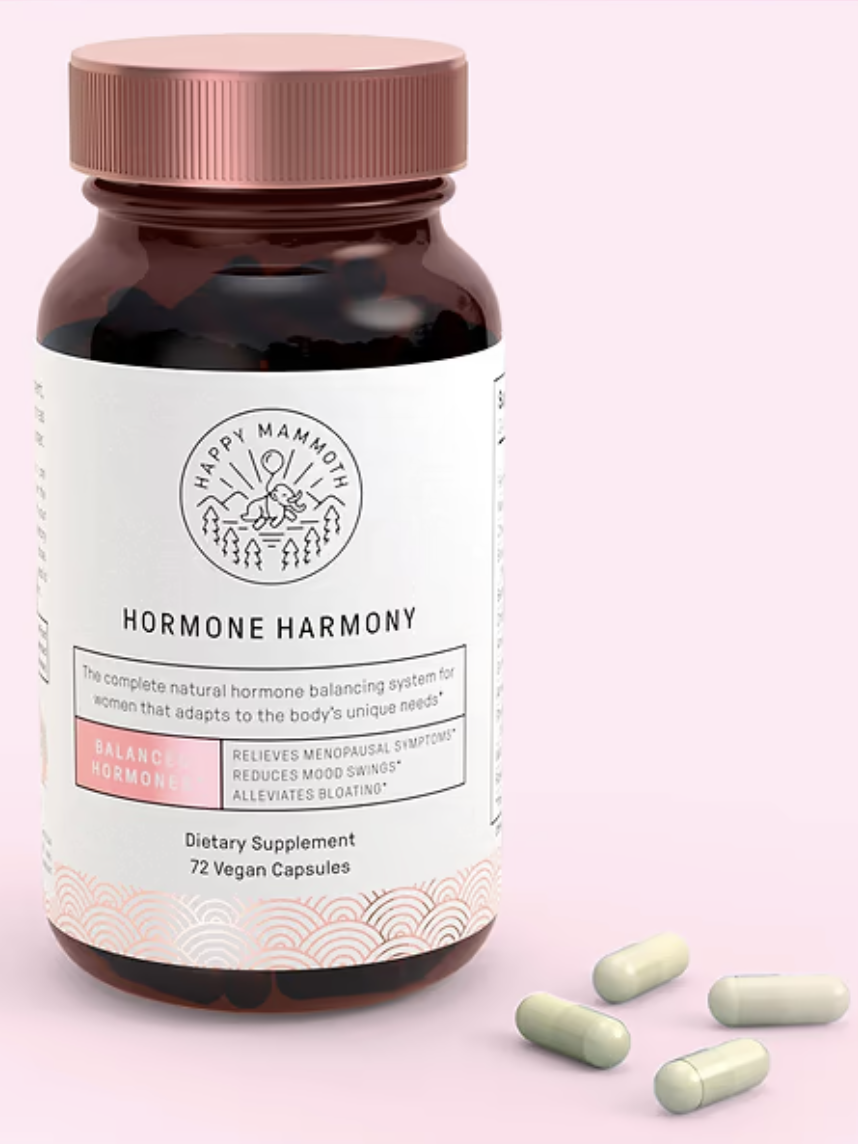 A bottle of "Happy Mammoth Hormone Harmony" dietary supplement with 72 vegan capsules, shown alongside three loose capsules, on a pink background.