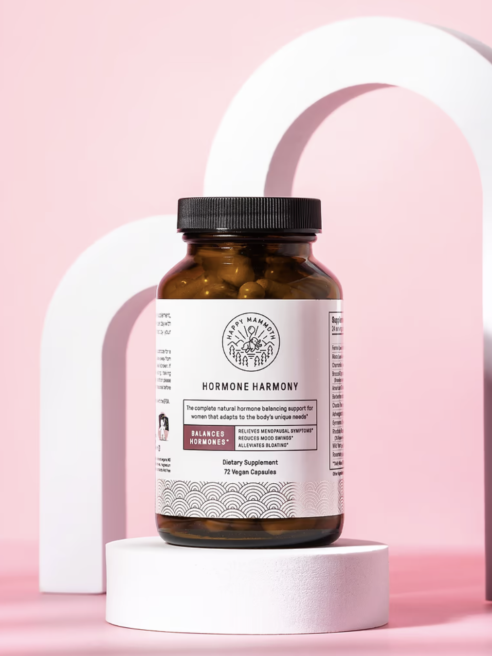 A bottle labeled "Hormone Harmony" with 72 vegan capsules is placed on a round white pedestal against a pink background with abstract white arch shapes.