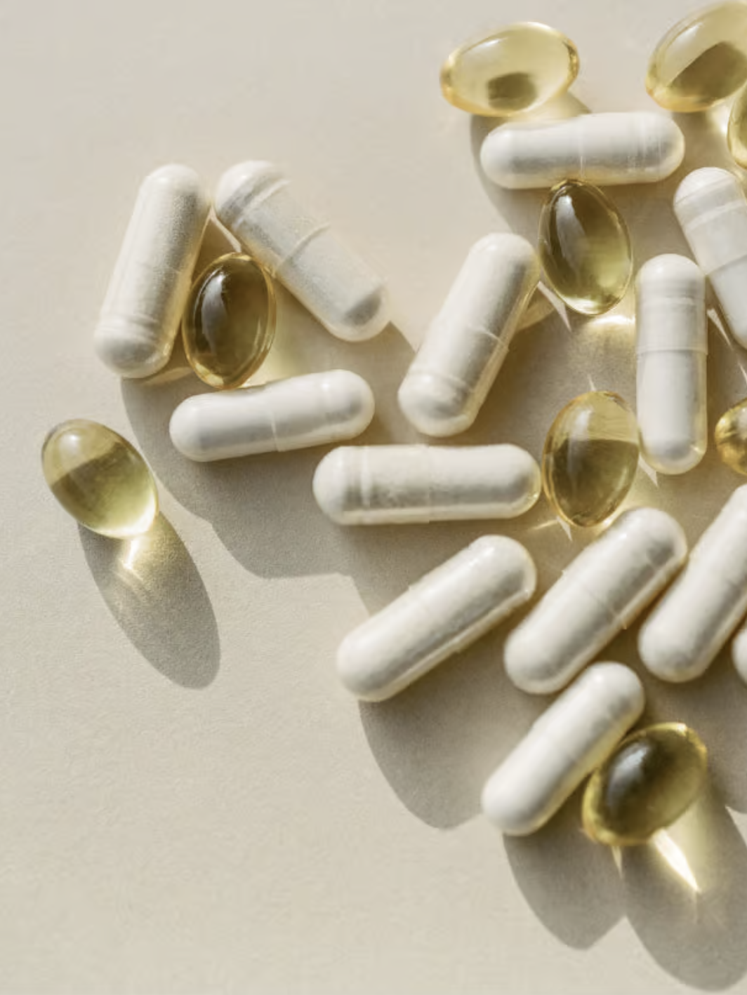 White capsules and yellow translucent gel pills scattered on a light surface.