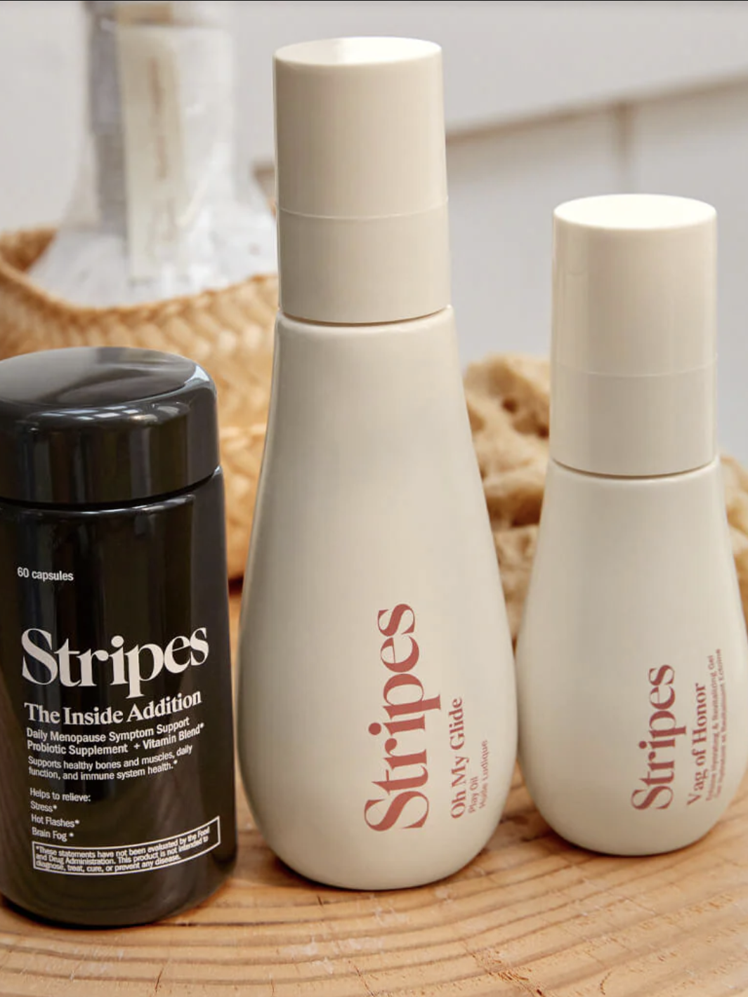 Three skincare products from "Stripes" on a wooden surface, including a black bottle labeled "The Inside Addition" and two white bottles labeled "On My Knees" and "The Full Monty.
